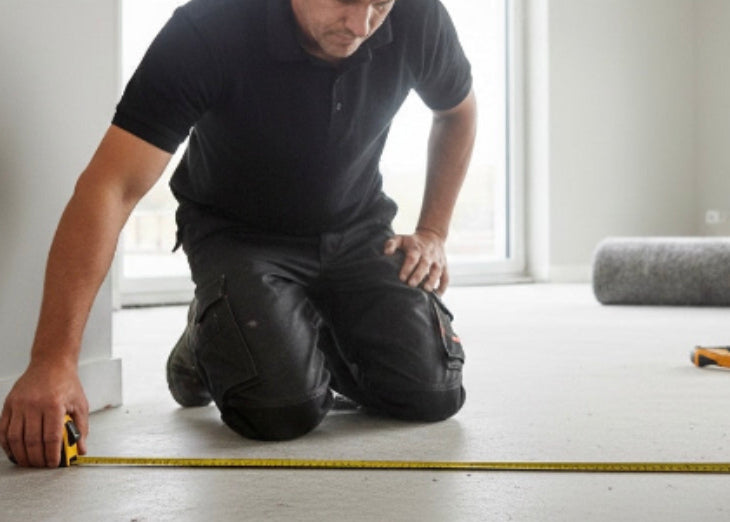 Man measuring floorboards in a room with large windows
